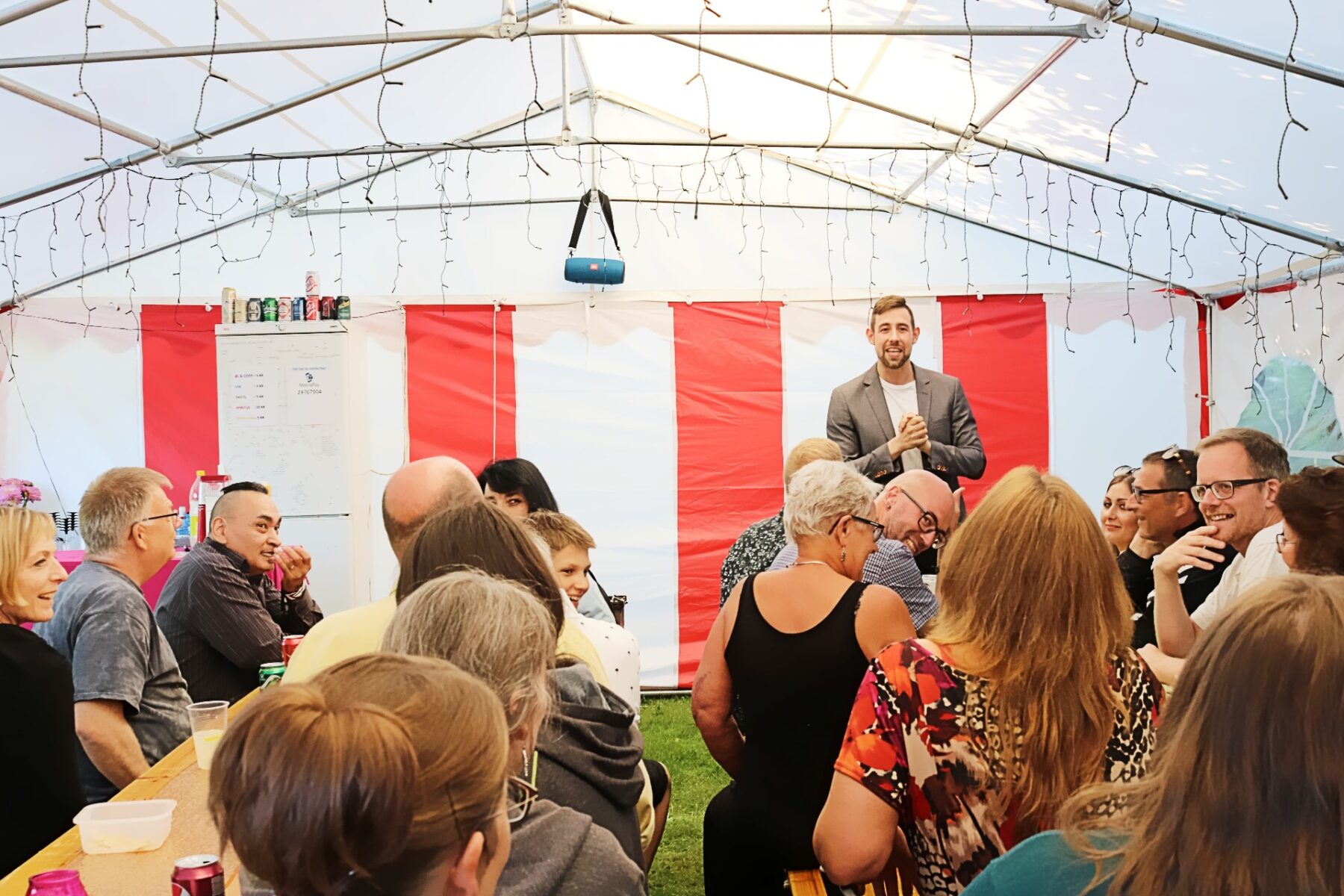 Mand står foran et publikum i et telt med hvide og røde striber