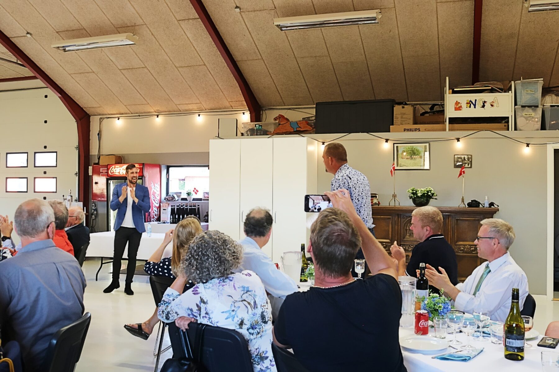 To mænd står foran et publikum, og den ene mand laver tryllekunstner på den anden