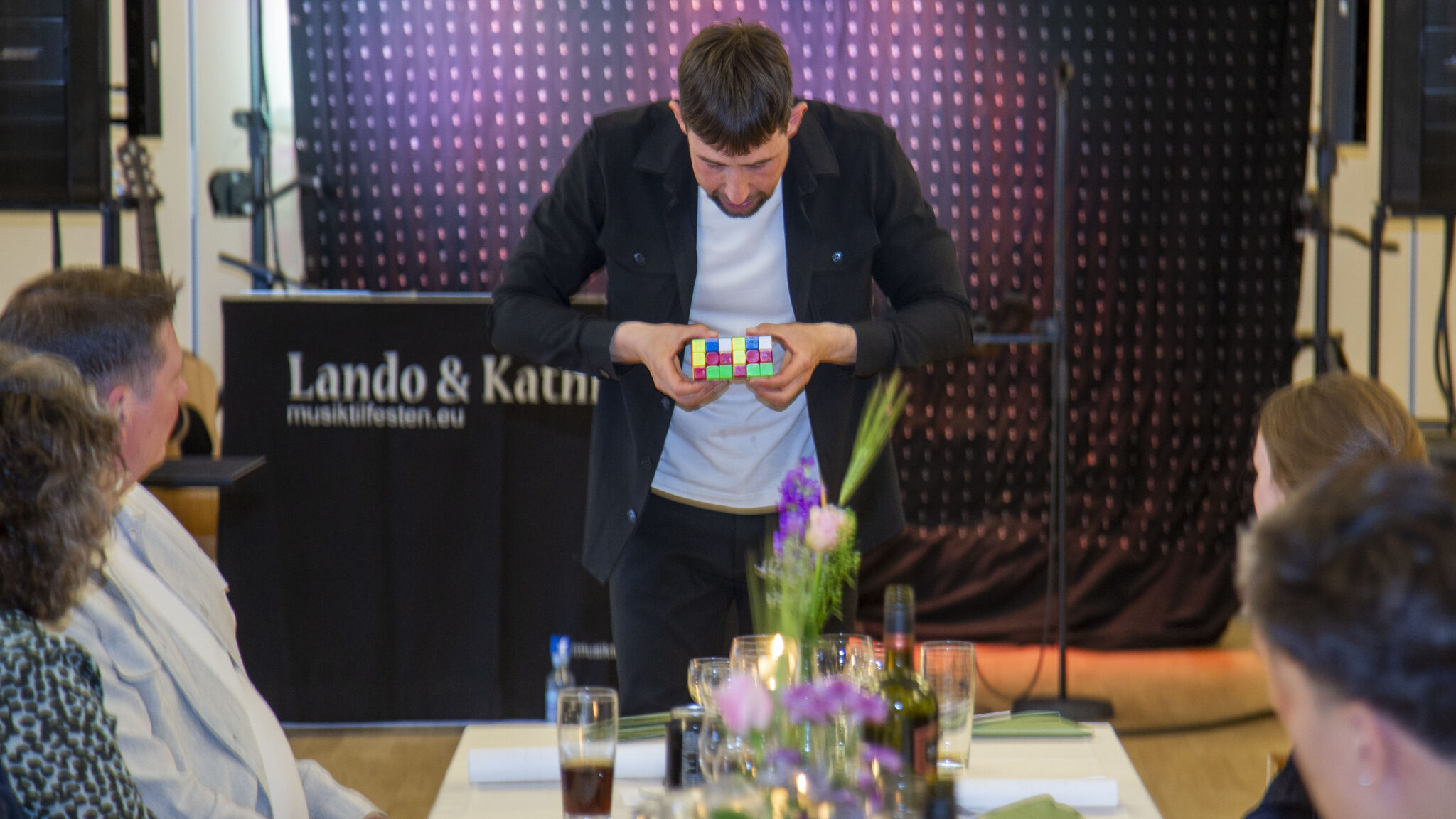 Tryllekunstner Nicolaj Mogensen løser en Rubiks terning foran et publikum ved et arrangement.